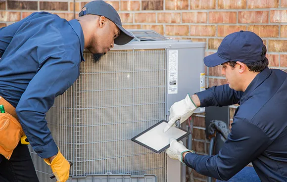 Two HVAC technicians working on an air conditioning unit, showcasing professional service.